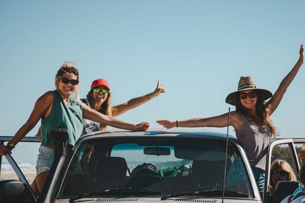 Excursiones de Australia tres chicas subidas en el coche sonriendo a cámara y el cielo despejado